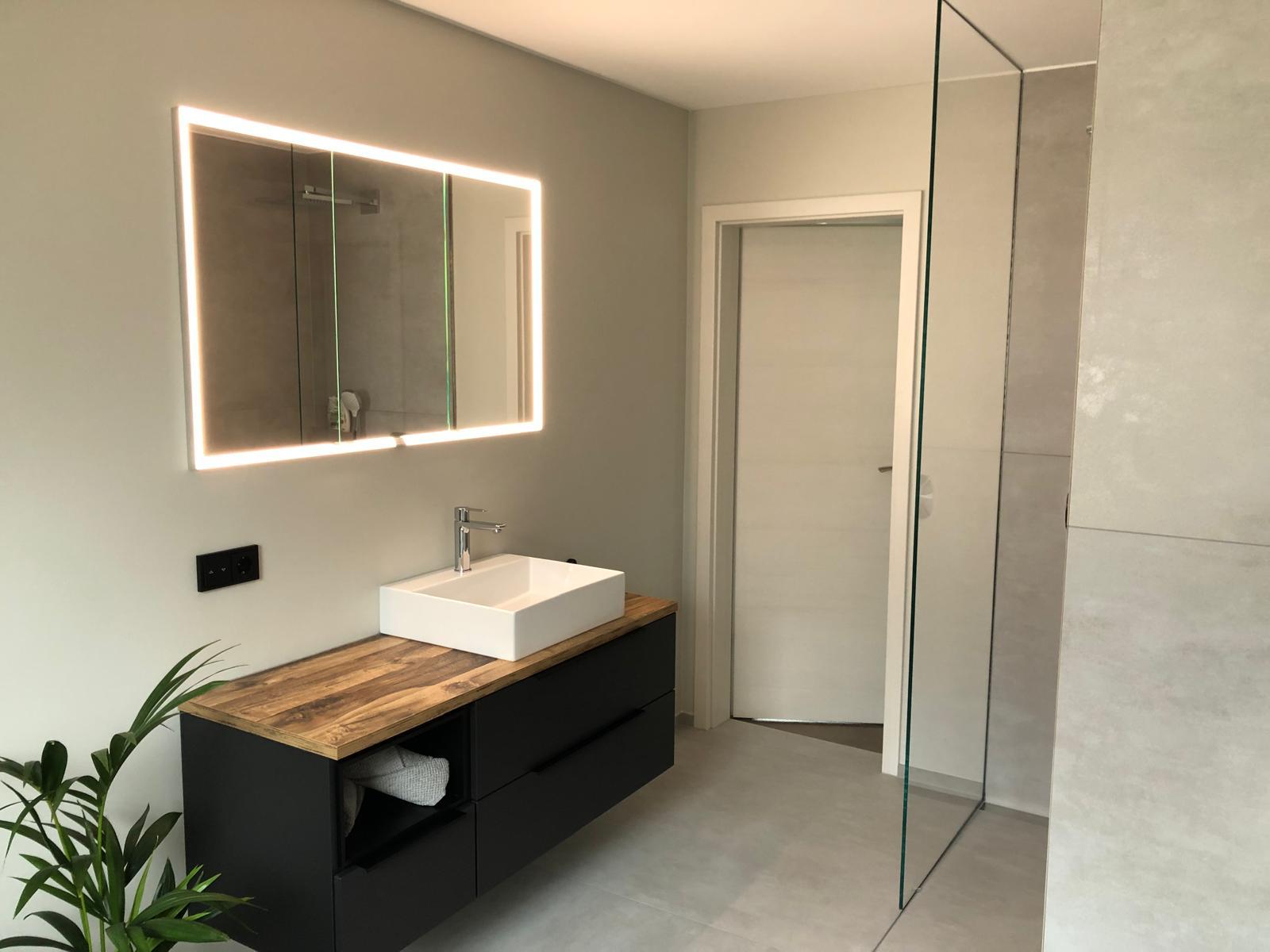 Moderner Waschtisch mit LED-Spiegel und angrenzender Dusche